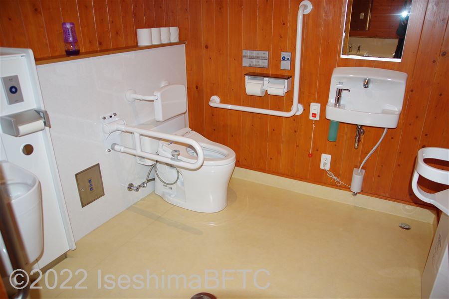 創造の森横山作業所　車いす対応トイレ内部　入口からみて左奥に、よこ置きに便器。入口正面に洗面台